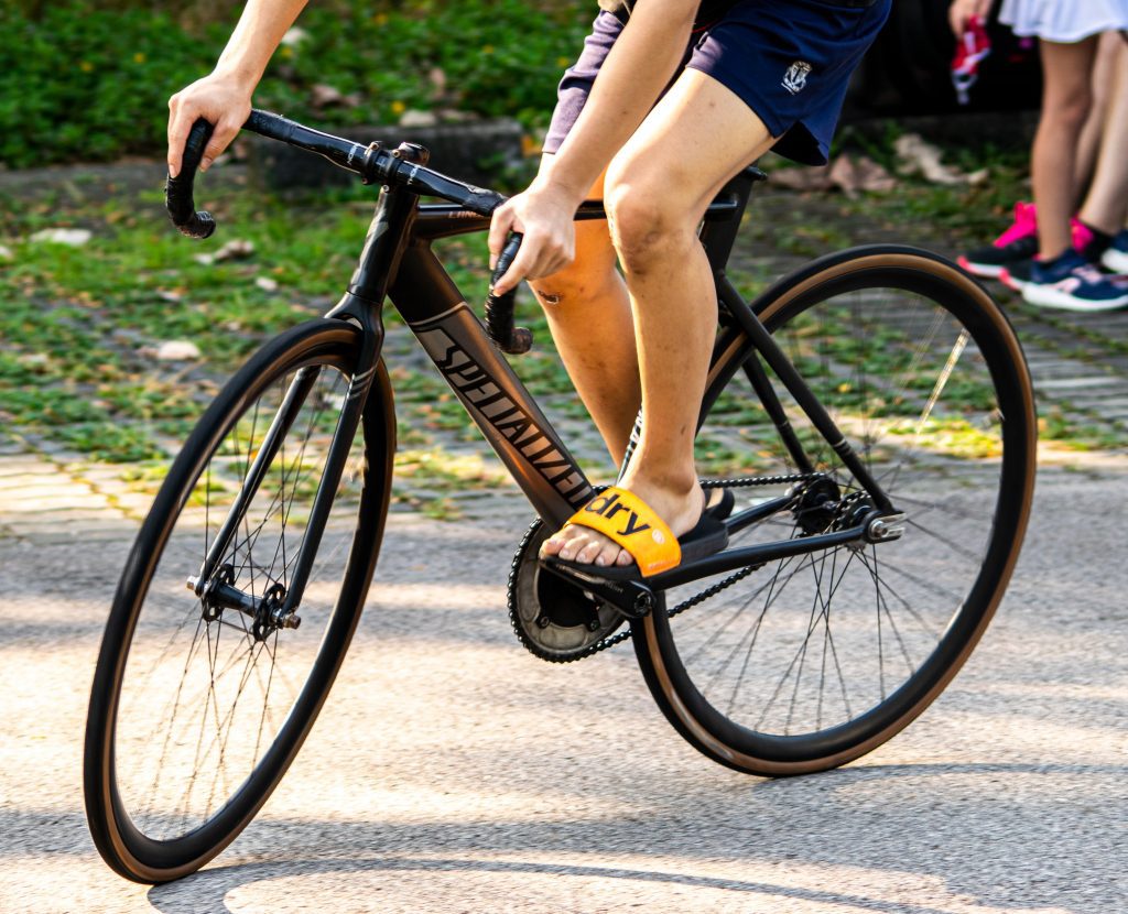 Image in a post titled 'what is fixed-gear freestyle? (and why track riders think it's stupid)' | closeup of a bicycle with a cyclist | fixed gear focus Closeup of a bicycle with a cyclist. Source: unsplash